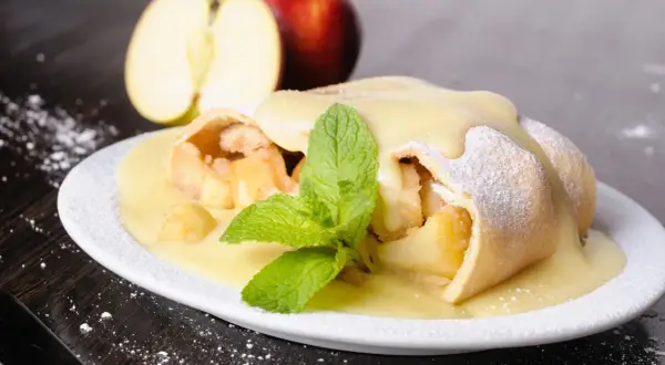 Ein köstlicher Apfelstrudel, übergossen mit Vanillesauce und garniert mit Minze. Perfekt für ein Apfelstrudel Rezept.