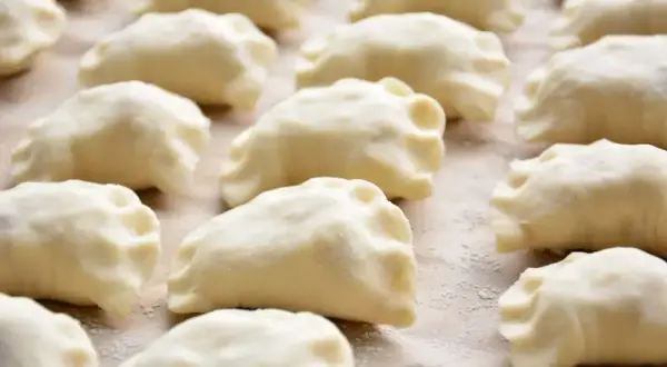 Gotowe do gotowania ciasto na pierogi, ułożone rzędami na blacie.