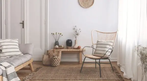 Un angolo del salotto arredato con un divanetto in legno, una poltrona in rattan, tappeto in juta e decorazioni naturali. Ecco come riempire un angolo del salotto con stile.
