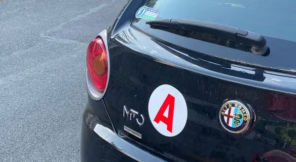 Autocollant "A" sur une Alfa Romeo noire, signe d'un jeune conducteur. La voiture a 140 ch.