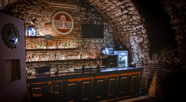 Wnętrze "House of Beer" z kamiennymi ścianami, barem pełnym butelek i kranów piwnych.