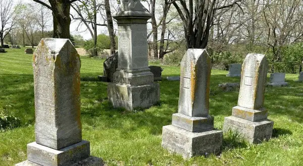 Vieilles pierres tombales dans un cimetière verdoyant, sous des arbres feuillus. Un lieu paisible pour se souvenir.