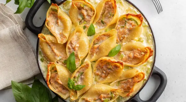 Un plat de conchiglioni farcis, dorés et garnis d'une farce savoureuse, baignant dans une sauce crémeuse et décorés de feuilles de basilic frais.