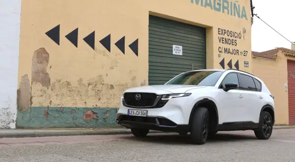Vit Mazda CX-5 framför en sliten gul byggnad med svarta pilar. Kanske ett Mazda CX-5 problem med att hitta rätt väg?