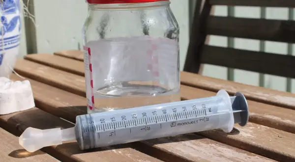 En spruta med koksaltlösning för barn står bredvid ett glas med vatten.