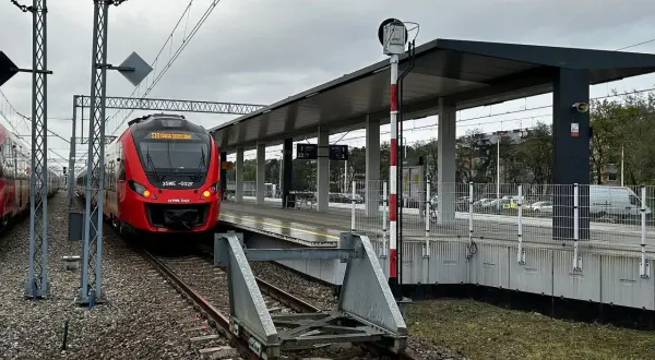 Czerwony pociąg PKP SKM stoi na peronie. W tle nowoczesna wiata i słup sygnalizacyjny.