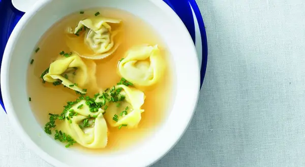 Eine Schüssel mit Tortellini in Brühe, garniert mit Schnittlauch.