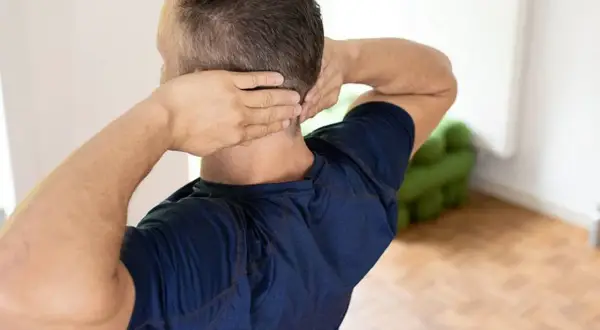 Mann mit Händen im Nacken, der sich fragt: nackenschmerzen wann zum arzt.