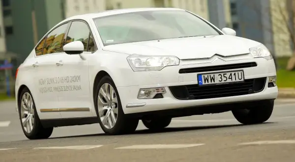 Biały Citroen C5 2.0 HDi z napisem "NOWY SILNIK 3.0 V6 HDi 240KM" na drzwiach, jadący po drodze.
