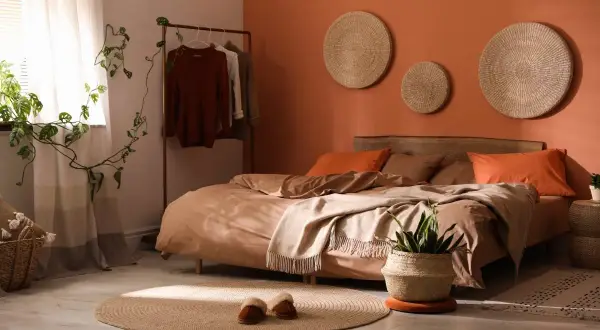 A cozy bedroom with bold colors like terracotta and rust. A bed with earthy-toned linens, a plant, and woven wall art.