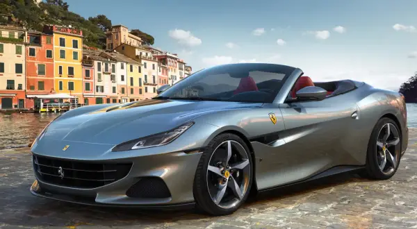 Srebrny Ferrari Portofino z czerwonym wnętrzem na tle kolorowych budynków nad wodą.