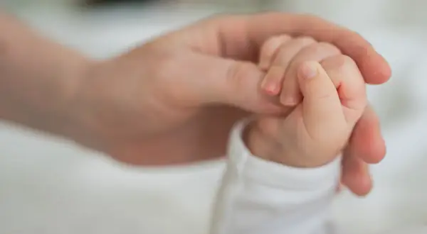 Dłoń rodzica obejmuje maleńką dłoń dziecka. To symbol miłości i wsparcia, a także świadczenie rodzicielskie.