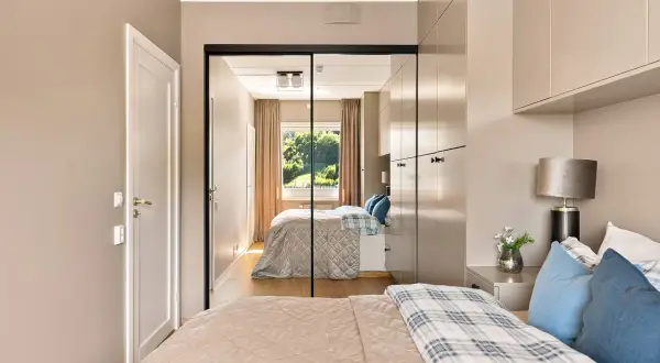 Ein großer spiegel im schlafzimmer reflektiert das Bett, die Vorhänge und das Fenster mit Blick ins Grüne.