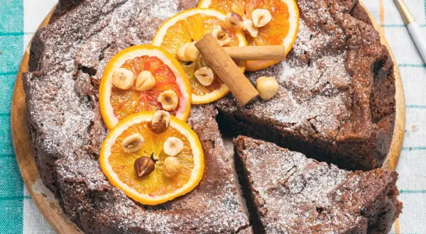 Torta di pane ricetta della nonna, cosparsa di zucchero a velo, decorata con fette d'arancia, nocciole e cannella.