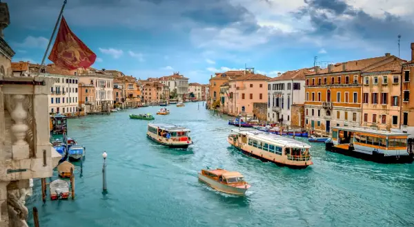 El Gran Canal de Venecia, con barcos y vaporetos, muestra cómo moverse por Venecia. Edificios coloridos flanquean el agua turquesa.