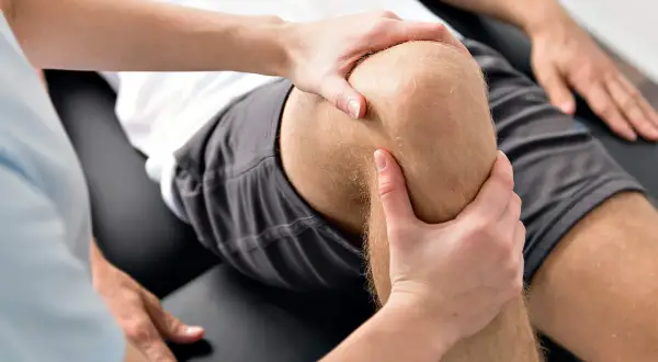 Physiotherapeut untersucht das Knie eines Mannes, um Probleme mit dem hinteren Kreuzband zu identifizieren.