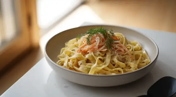 Un plato de pasta fettuccine con una cremosa salsa, coronado con hebras de salmón ahumado y eneldo fresco.