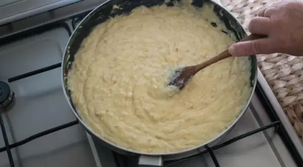 Masa de croquetas cremosa en sartén, removida con cuchara de madera.