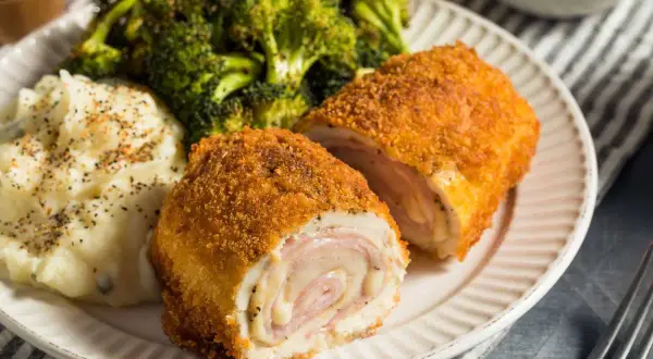 Un delicioso cordon bleu, crujiente por fuera y jugoso por dentro, acompañado de puré de patatas y brócoli.