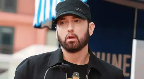 Eminem, znany jako "mockingbird po polsku", w czapce i z brodą, przemawia do mikrofonu.