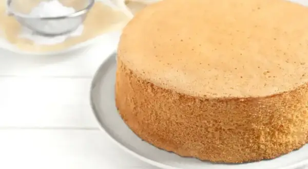 Idealny biszkopt, by wyszedł puszysty, piecz w temperaturze 170-180°C. Na talerzu leży złocisty biszkopt, obok sitko z cukrem pudrem.