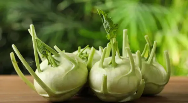 Mehrere kleine Kohlrabi-Knollen mit grünen Blättern liegen auf einem Holztisch.