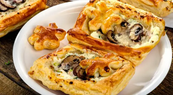 Chrupiące ciasto francuskie z pieczarkami i serem, podane na białym talerzu. Idealne na przekąskę.