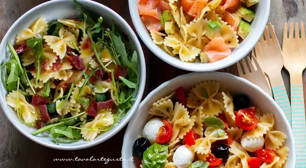 Tre idee per cosa mettere nella pasta fredda: farfalle con rucola e prosciutto, salmone e avocado, o pomodorini, mozzarelline e olive.