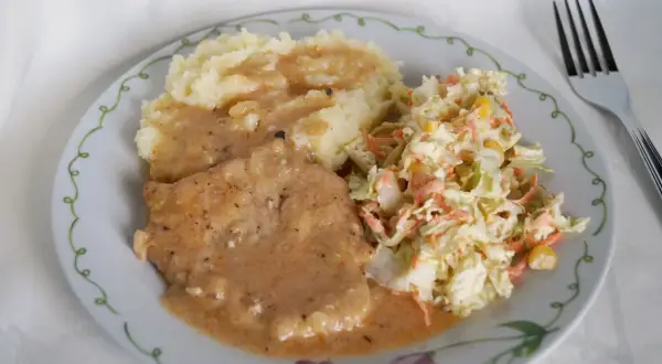 Schab duszony z cebulą w sosie własnym, podany z puree ziemniaczanym i surówką z kapusty. Pyszny, domowy obiad.