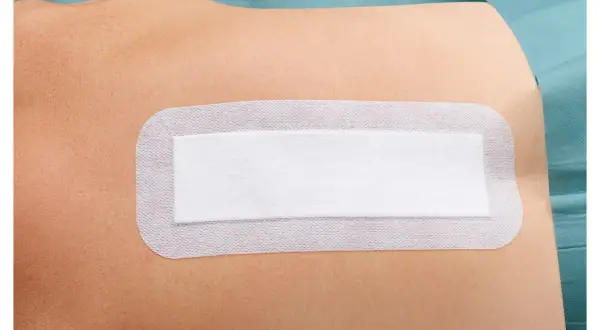 Biały, sterylny plaster na skórze, chroniący ranę po operacji. Zapewnia komfort i bezpieczeństwo podczas rekonwalescencji.