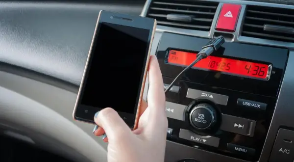 Ręka trzyma smartfon, podłączony kablem do radia samochodowego. Dowiedz się, jak połączyć się z transmiterem.