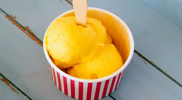 Un refrescante helado de mango en un recipiente a rayas rojas y blancas, listo para disfrutar en un día caluroso.