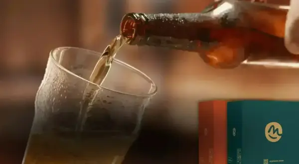 Versando una hefe birra dorata in un bicchiere bagnato. Sullo sfondo, due scatole colorate con il logo "m".