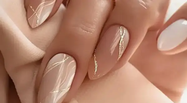 Elegancki, modny manicure w odcieniach beżu i bieli, ozdobiony złotymi, falistymi liniami.