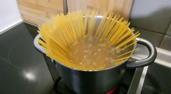 Długie, żółte spaghettini gotują się w garnku na kuchence.