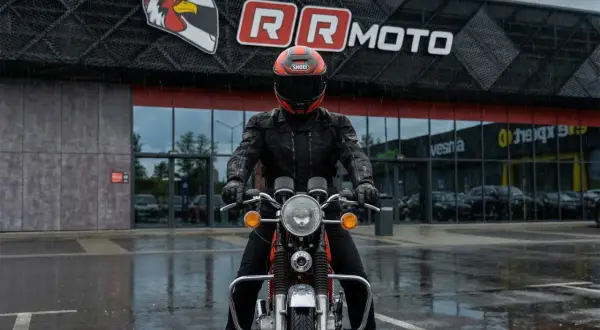 Motocyklista w kurtce z membraną, która chroni przed deszczem, przed budynkiem RR MOTO.