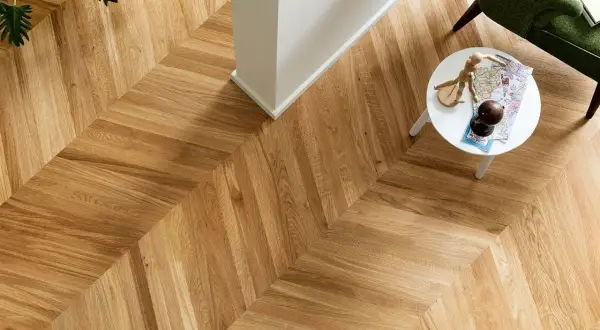 Un elegante parquet a spina di pesce, con un tavolino bianco e una poltrona verde. Per mantenere la sua bellezza, chiediti ogni quanto lavare il parquet.