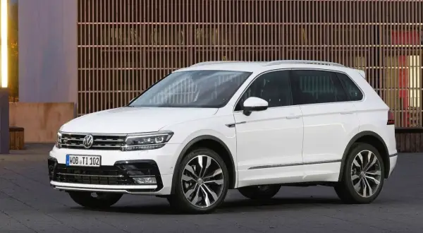 Biały Volkswagen Tiguan na tle nowoczesnej fasady. Wiele osób szuka **volkswagen tiguan opinie** przed zakupem.
