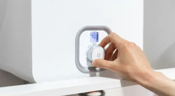 Mano che gira la manopola per spegnere la caldaia a condensazione. Display digitale mostra 48°C.