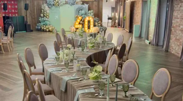 Eleganckie przyjęcie weselne na 40 osób. Stoły nakryte, ozdobione kwiatami i świecami. W tle dekoracje z balonów i podświetlana liczba 40.