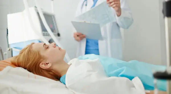 Kobieta w śpiączce leży podłączona do respiratora, lekarz analizuje jej wyniki.