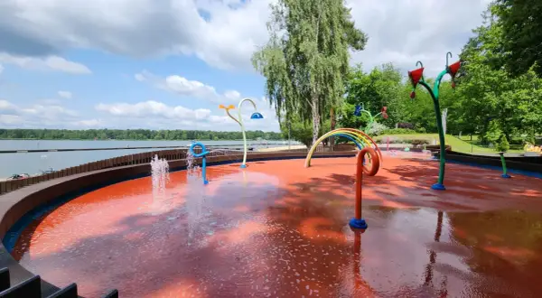 Kolorowy plac zabaw wodnych przy Jeziorze Paprocany, z fontannami i tęczą, zaprasza do zabawy w upalny dzień.