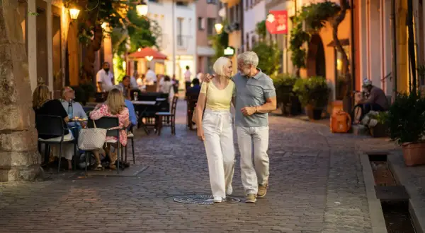 Ein älteres Paar spaziert abends durch eine Gasse in Freiburg. Was kann man in Freiburg machen? Hier: gemütlich essen gehen und die Atmosphäre genießen.