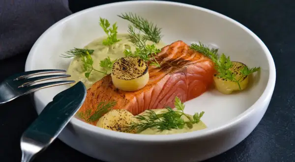 Un délicieux saumon à la toscane, servi avec une sauce crémeuse, des pommes de terre grillées et des herbes fraîches.
