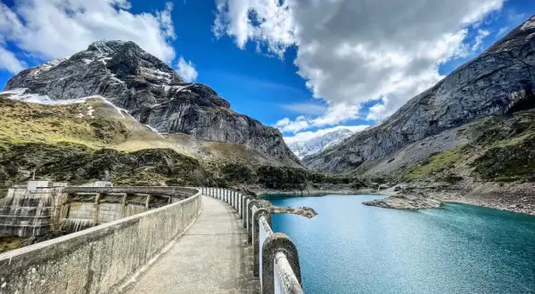 Le cirque de Gavarnie lac, un barrage imposant domine un lac bleu turquoise, entouré de montagnes majestueuses sous un ciel nuageux.