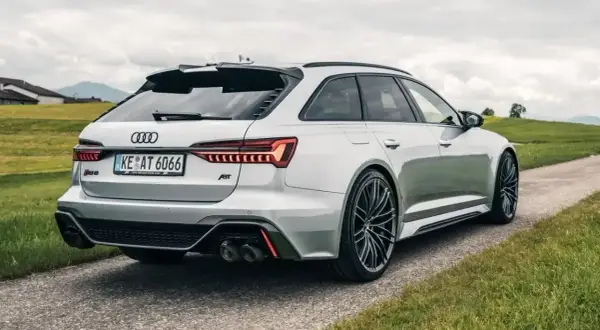 Białe Audi RS6 C8 z pakietem ABT na tle zielonych wzgórz. Widok z tyłu na sportowe detale i felgi.