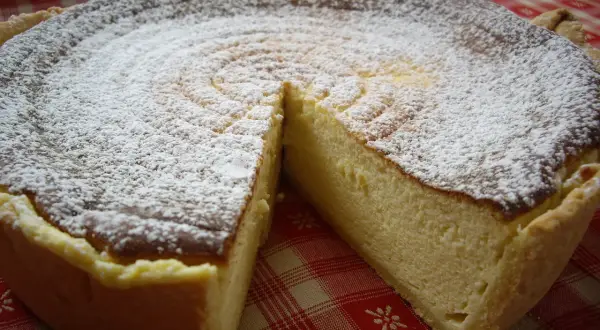 Une délicieuse tarte au fromage blanc, saupoudrée de sucre glace, prête à être dégustée sur une nappe à carreaux rouges.