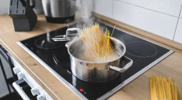 Spaghetti kochen in einem Topf auf dem Herd. Ein Bündel Spaghetti liegt daneben. Der Trick, wie viel Spaghetti pro Person, ist hier visuell dargestellt.