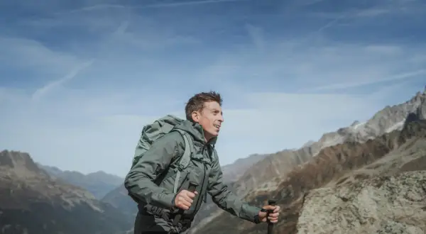 Mężczyzna z plecakiem i kijkami trekkingowymi wędruje po górach, podziwiając widok na masyw Mount Blanc.