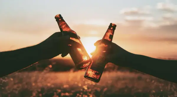 Due mani brindano con due bottiglie di birra al tramonto, un meritato momento di relax dopo un allenamento.